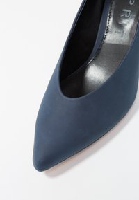Chaussure à talon haut bleue en matériau synthétique lisse, avec un bout pointu et un design minimaliste sans motifs ou accents remarquables.