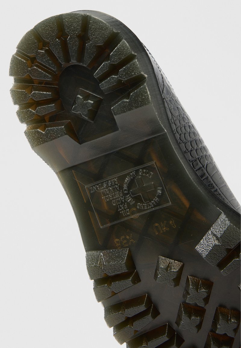 Zwarte rubberen schoenzool met een gestructureerd loopvlakpatroon voor grip, met een centraal logo en ingebouwde details voor constructie en duurzaamheid.