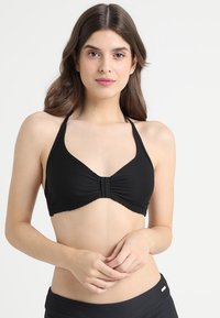 Zwarte bikini top met een geribbelde textuur, halternek ontwerp en een gedraaide voorkant. Zachte stof en minimalistische stijl.