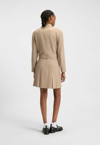 Beige pinstriped dress with long sleeves, fitted waist, pleated skirt hem, and back zipper. Worn with black shoes and white socks.