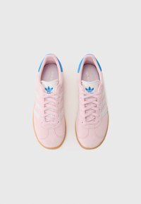 Rosa mockaskinnssneakers med vit tre-stripesdesign, blå detaljer på tungan och en texturerad gummisula. Snörningen är i matchande rosa.