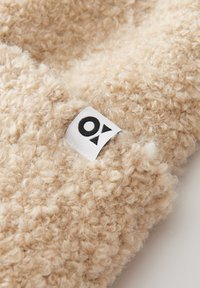 Tessuto beige con texture e aspetto morbido. Presenta un piccolo etichetta bianca con lettere nere. La texture è evidente, morbida e accogliente.
