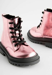 Bottes métalliques roses jusqu'à la cheville avec des lacets noirs, surface texturée, bout rond et semelle en caoutchouc noire épaisse présentant un motif de semelle.