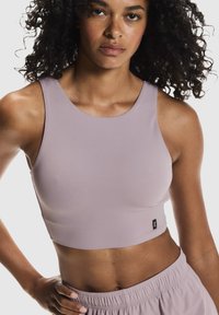 Haut court de sport violet clair avec un col rond et un design sans manches. Tissu lisse et extensible ; comporte une petite étiquette de marque en bas.