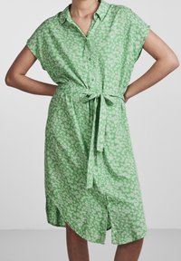 Grön knäppklänning med korta ärmar, åtsittande midjeband, blommönster, mjukt tyg och asymmetrisk nederkant.