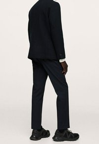 Czarny dopasowany żakiet z teksturowanej tkaniny, w połączeniu z ciemnymi spodniami i półformalnymi czarnymi sneakersami, widok z tyłu.