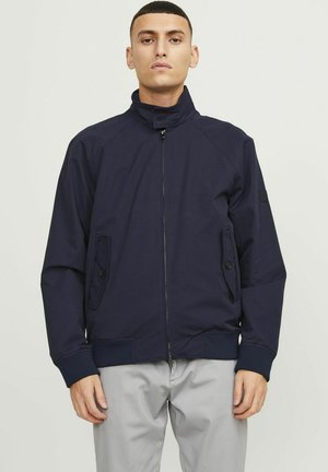 Marineblauwe ritsjack met hoge kraag, voorzakken en geribbelde manchetten. Kenmerkt zich door een gladde stof en een gestructureerde pasvorm.