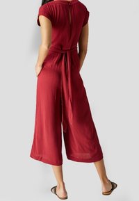Rode, losse jumpsuit met korte mouwen, een strik taille en een keyhole detail achter. Gemaakt van lichtgewicht, gestructureerde stof.