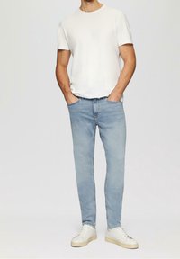 Jean bleu clair coupe slim, associé à un t-shirt blanc à col rond et des baskets blanches. Design simple, sans motifs ni accents visibles.