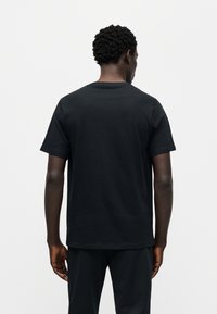 Μαύρο βαμβακερό t-shirt με κοντά μανίκια και λαιμόκοψη τύπου crew, που παρουσιάζει απλό σχεδιασμό και μαλακή υφή, φαίνεται από πίσω.