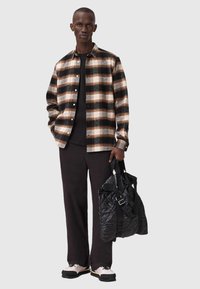 Camicetta di flanella a scacchi con colori marrone, nero e crema, t-shirt nera, pantaloni neri larghi e una borsa nera strutturata.