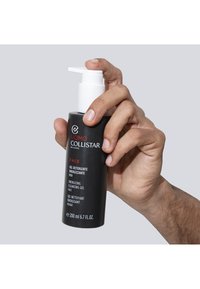 Czarna cylindryczna butelka z białą pompką, oznaczona napisem "Energetyzujący żel do mycia twarzy". Posiada wielojęzyczny tekst i matowe wykończenie.