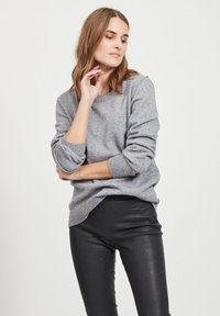 Un pull en laine gris avec un col rond et des poignets côtelés, associé à un pantalon en cuir noir, créant une tenue décontractée.
