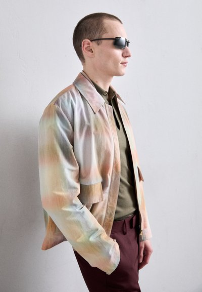Giacca leggera e multicolore con un delicato motivo a gradiente, caratterizzata da un colletto classico e apertura frontale, indossata sopra una camicia verde oliva uniforme.