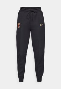Pantalon de jogging noir avec taille élastique et cordon, avec le logo Nike doré sur la cuisse droite et le blason du FC Barcelone sur la cuisse gauche.