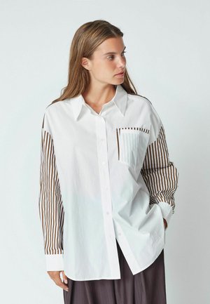 Camicia bianca con maniche lunghe a righe marroni, una tasca sul petto e chiusura con bottoni. Realizzata in un tessuto leggero con una consistenza liscia.