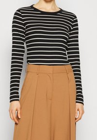 Maglia a maniche lunghe bianca e nera a righe con scollatura rotonda, abbinata a pantaloni beige a vita alta con pieghe e tasche laterali.