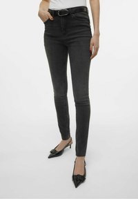 Jeans ajustados negros con cintura alta, que incluyen un cinturón, textura suave y un ligero desgaste; combinados con tacones de tipo slingback negros.