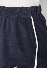 Marineblaue Frottee-Shorts mit elastischem Bund, ausgestattet mit weißen Seiteneinfassungen und einer Textur, die Weichheit und Saugfähigkeit vermittelt.