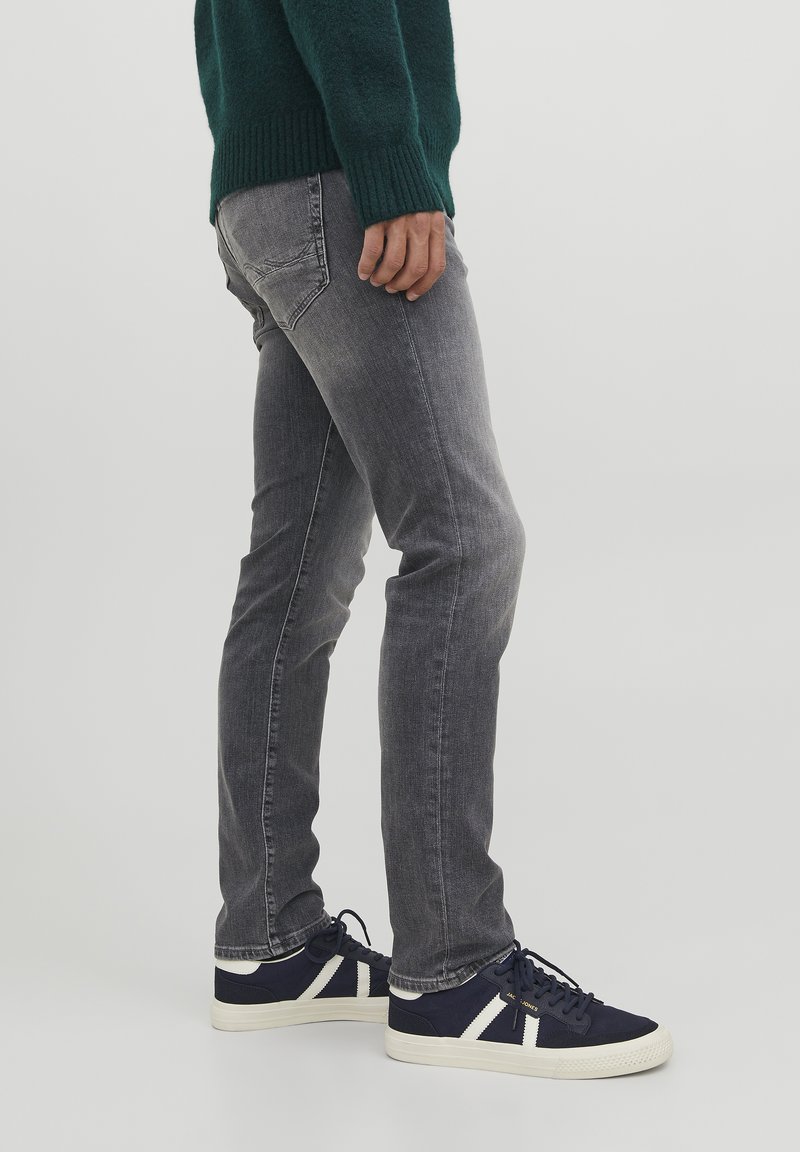 Jeans de denim gris con un corte ajustado y un ligero desgaste. Combinados con zapatillas navy que tienen detalles en blanco y una tela texturizada.