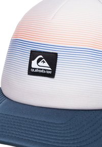 Gorra con parte superior blanca y a rayas multicolores en tonos de naranja y azul. Visera azul marino, tejido texturizado y un parche de logo negro.