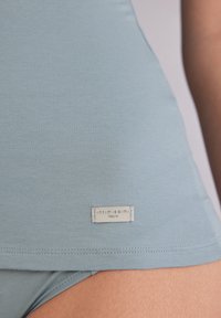 Ljusblå tanktopp i mjukt tyg, med en sydd fåll och en liten märkesetikett med "intimissimi" och "Naturai."