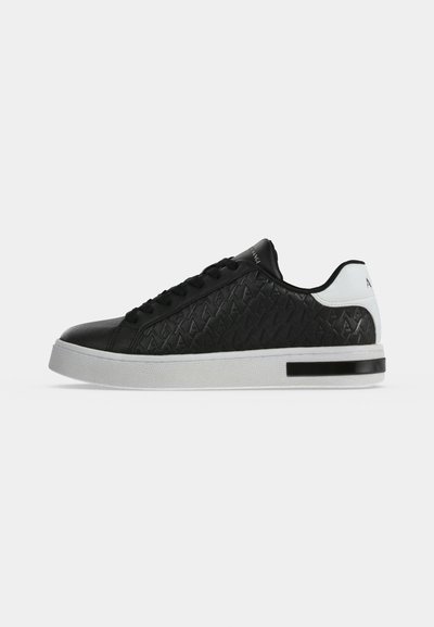 Basket noire à lacets et à motifs, avec un empiècement blanc au talon et une semelle blanche épaisse, présentée de profil sur un fond uni.