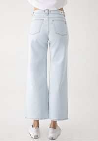 Jeans de pierna ancha color azul claro, elaborados en denim, con una cintura alta, dos bolsillos traseros y un dobladillo limpio. Combinados con zapatillas blancas.