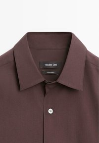 Chemise marron foncé à col avec un bouton blanc visible et une étiquette de la marque "Massimo Dutti" à l'intérieur de l'encolure.