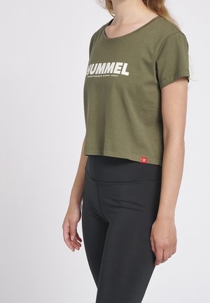 Olivengrøn croppet t-shirt med rund halsudskæring, med hvidt mærkelogo trykt på fronten. Kombineret med sorte leggings.