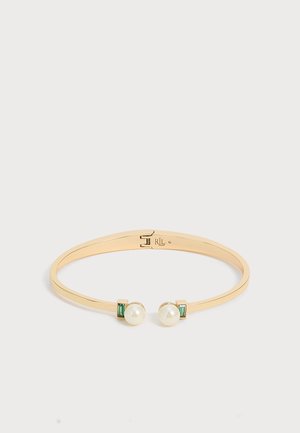 Bracelet jonc ouvert doré avec deux perles blanches et de petites pierres rectangulaires vertes à chaque extrémité sur un fond clair uni.