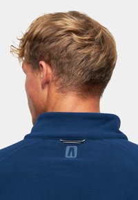 Granatowy polar z wysokim kołnierzem, z dyskretnym logo i dekoracyjnym przeszyciem w okolicy szyi. Miękka tekstura i dopasowany krój.