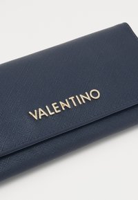 Portafoglio texture navy con il logo dorato "VALENTINO" sul fronte. Presenta una forma rettangolare elegante e bordi lisci.