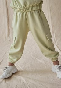 Lys grønne joggerbukser med elastisk talje, side cargo-lommer og tapered manchetter, parret med hvide sneakers og rosa ankelstrømper.