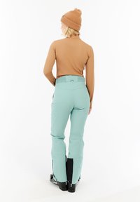 Skikleding met een bruin langemouwen top en muntgroene broek met een rekbare tailleband, zwarte accenten en ritsmanchetten.