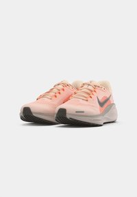 Une paire de chaussures de course Nike roses claires avec un logo swoosh gris et une semelle rembourrée, présentée sous un angle bas à l'avant sur fond blanc.