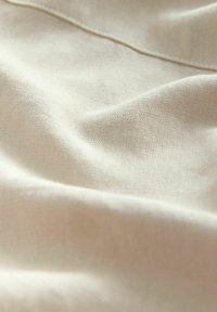 Lichtbeige stof met een zachte, gestructureerde oppervlakte, met subtiele weefdetails en zachte plooien. Ideaal voor textiel en stoffering.