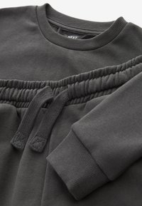 Dunkelgrauer Sweatshirt mit rundem Halsausschnitt, elastischem Bund mit verstellbarem Kordelzug und gerippten Bündchen. Glatte Textur und minimalistisches Design.