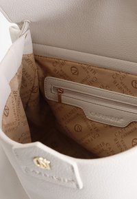 Valkoinen nahkakäsilaukku, jonka sisäosa on vaaleankeltaista vuorikangasta, jossa on logo-kuviointi. Laukussa on vetoketjullinen tasku ja kultaiset aksentit.