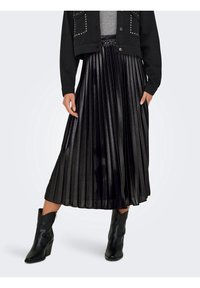 Falda negra de tablas con un brillo metálico, tejido ligero, cintura elástica, combinada con botines negros y una chaqueta negra corta.
