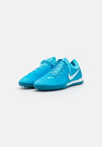 Pár jasně modrých běžeckých bot Nike s bílými swoosh logy a texturovanými gumovými podrážkami umístěnými na bílé ploše.