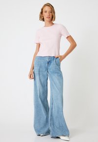 Lys pink stribet kortærmet top med en bølget kant, parret med vide lysblå denimjeans. Begge beklædningsgenstande har en afslappet pasform.