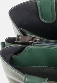 Nahaufnahme einer offenen grünen Ledertasche, die einen teilweise geschlossenen Metallreißverschluss im Inneren der Tasche zeigt.