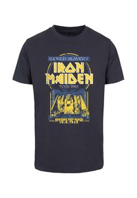 Svart bomull t-skjorte med gul og blå trykk med "Iron Maiden World Slavery Tour 1985," egyptiske motiver og konsertopplysninger.