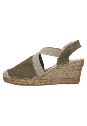 Zielone zamszowe sandały na koturnie z krzyżującymi się paskami, tekstylnymi akcentami, naturalnymi detalami z juty oraz zakrzywioną podeszwą koturnową dla stabilności.