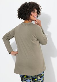Pitkähihainen oliivinvihreä paita, jossa on pyöreä kaula-aukko, suave rakenne ja rento malli, yhdistettynä kuviollisiin sinivihreisiin maastohousuihin.