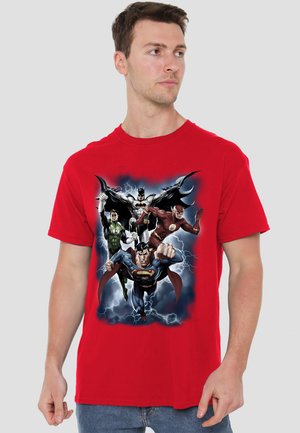 Man wearing a red T-shirt with flying superheroes Batman, Superman, Flash, and Green Lantern amid lightning on the front.