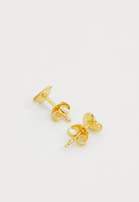 Pendientes de oro con acabado pulido, que presentan una base circular y acentos de diseño curvados. Diseño simple y ligero.