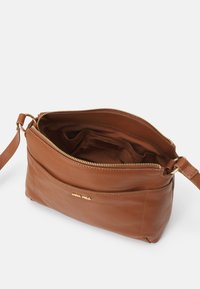 Brown leather crossbody bag with a textured exterior, gold zipper, and interior compartments. Features a logo on the front panel.