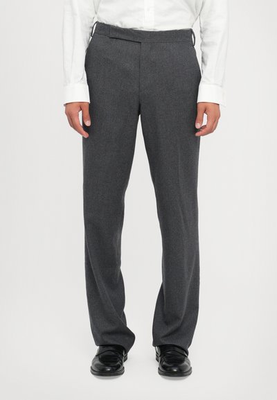 Pantalons tailleur gris en tissu texturé, avec une coupe droite, un devant plat et des poches latérales. Accompagnés de chaussures noires.